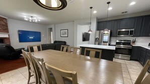 Une cuisine moderne avec des meubles de couleur sombre, des appareils en acier inoxydable et une table à manger en bois, assortie de chaises.
