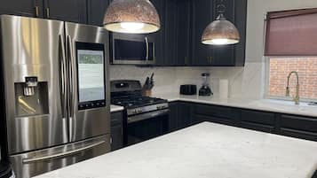 Una cocina moderna con electrodomésticos de acero inoxidable, encimera de mármol e iluminación colgante.