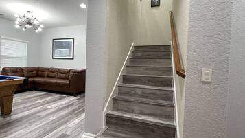 Una sala de estar moderna con un sofá de cuero marrón, una mesa de billar y una escalera con escalones de madera.