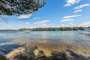 A clear lake with wooden docks and a forested shoreline. - Cozy Lakeside Retreat on Long Lake - Sleeps 4 (Traverse City)