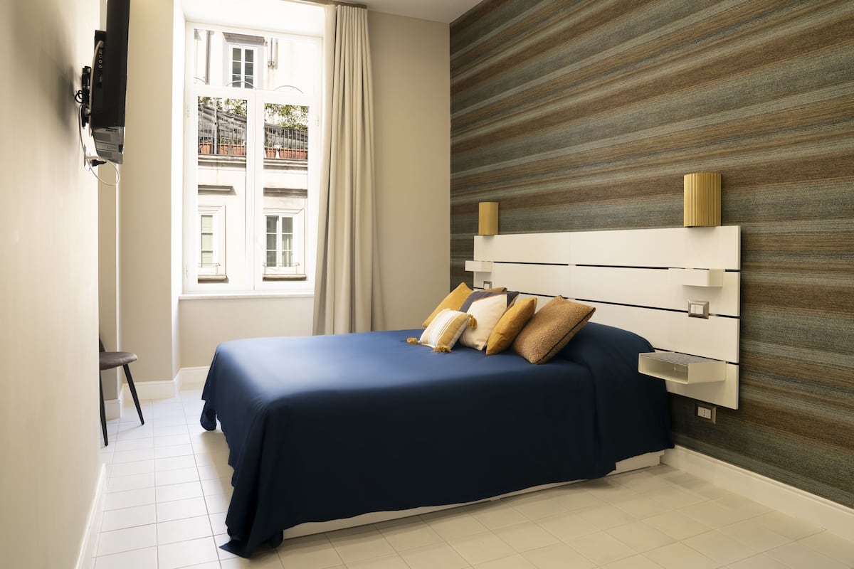 A modern bedroom with a large bed, a TV mounted on the wall, and a view of the outside through a window.