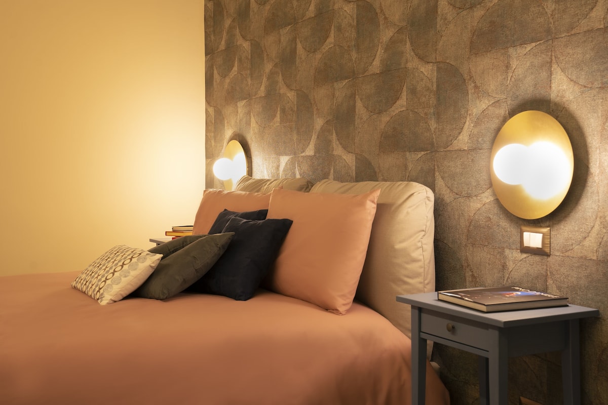 A bedroom with a bed, pillows, a bedside table, and a wall-mounted light fixture.