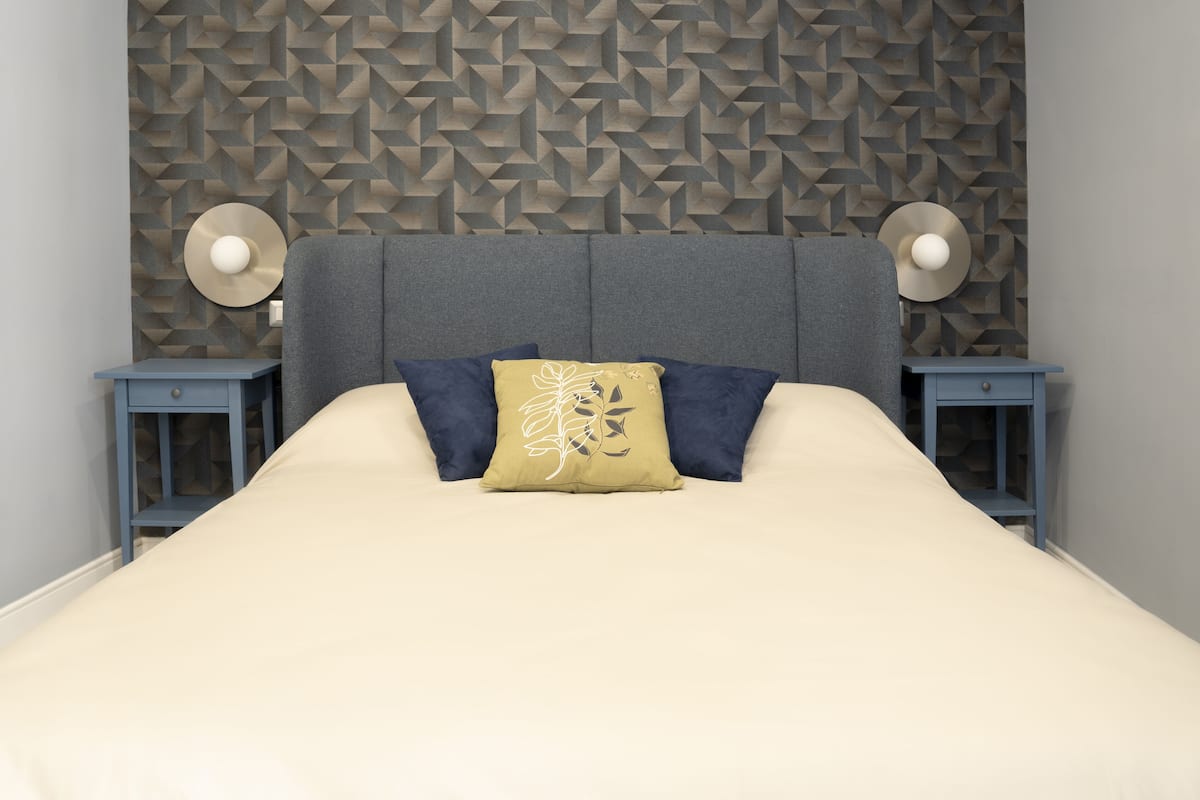 A bed with a geometric-patterned headboard, two bedside tables with lamps, and a single decorative pillow.