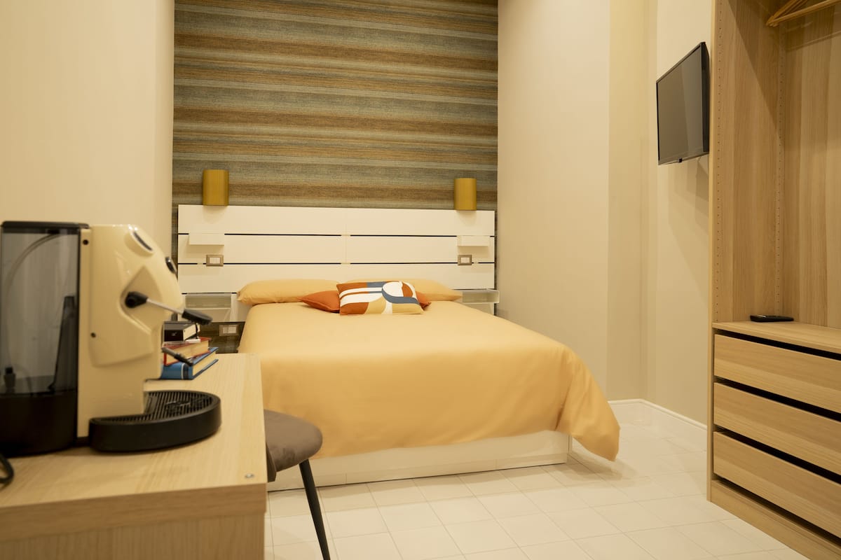 A hotel room with a bed, desk, chair, and a television mounted on the wall.