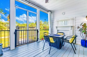 A covered patio with a table and chairs, a view of the outdoors, and a white wall with a clock.