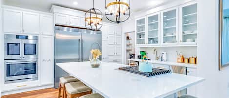 A modern kitchen with white cabinetry, stainless steel appliances, and a central island with stools.