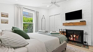 Un dormitorio con cama, chimenea, televisor y ventana con cortinas.