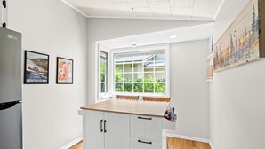 Una cocina con ventana, armarios blancos y un refrigerador.