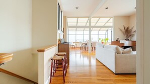 Amplia sala de estar con piso de madera, un sofá blanco y una mesa de comedor con sillas.