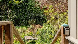 Una escalera de madera que da a un jardín con un patio empedrado y una verja de metal.