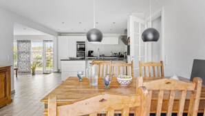 A modern kitchen with white cabinets, a dining area with a wooden table and chairs, and pendant lights. - Nice home in Sydals with WiFi (Sydals)
