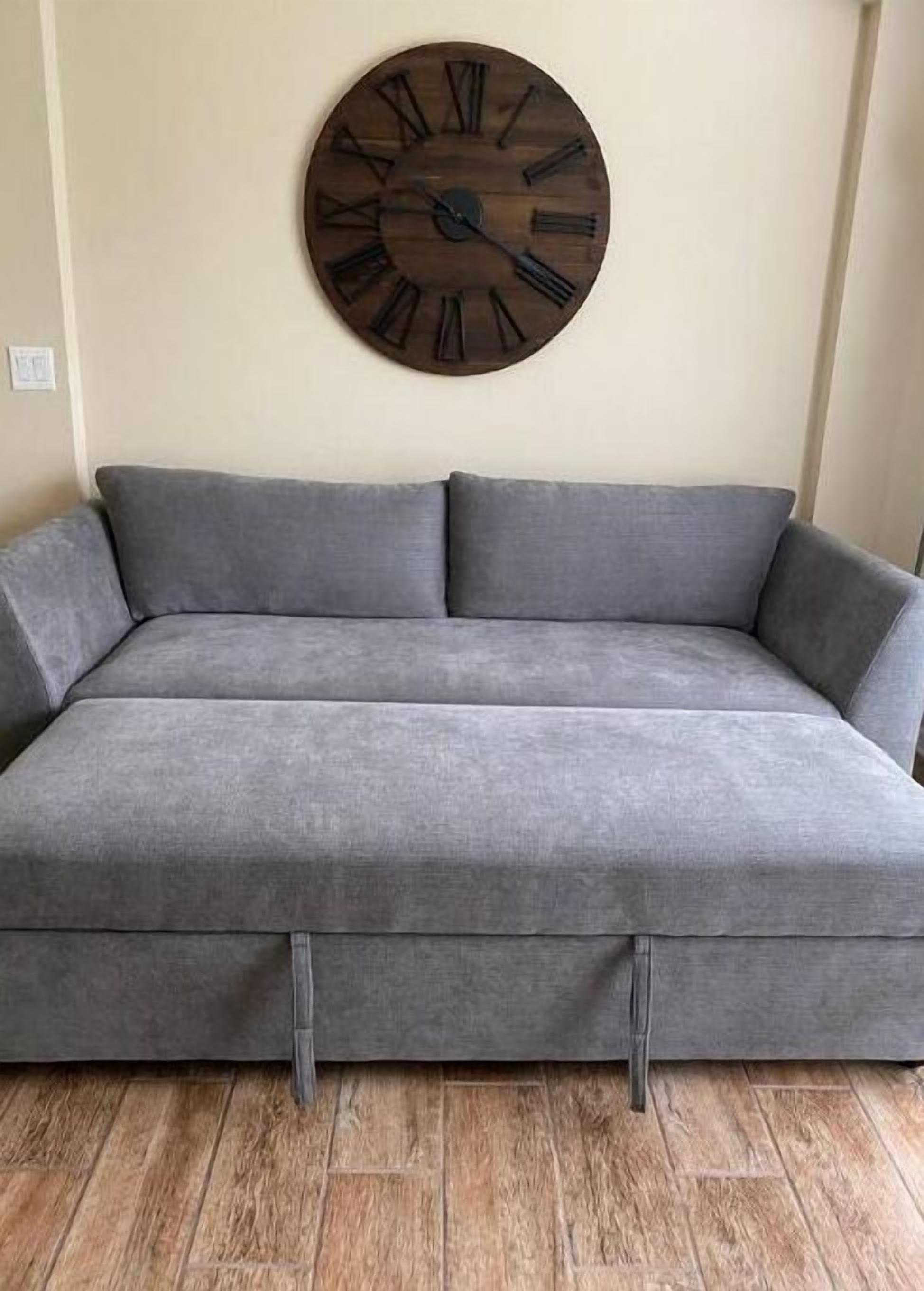A gray sofa with a wooden clock on the wall behind it.
