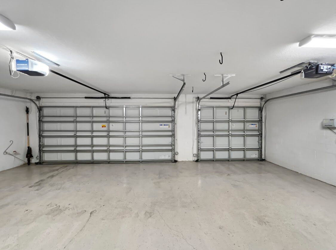 Un garage pulito e vuoto, con due porte metalliche, illuminazione al neon e pavimento in cemento.