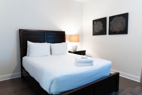 A neatly made bed with white linens and a folded towel, a bedside lamp, and two wall-mounted artwork pieces. - 7 miles to Disney. Spacious Villa with pool, spa, game room & Themed bedrooms. (Kissimmee)