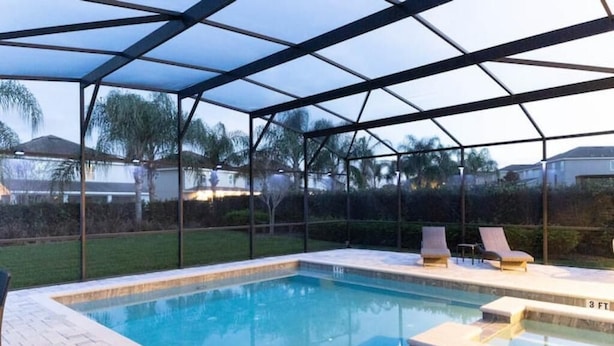 Une piscine dotée d’une structure en verre, de chaises longues et d’une terrasse carrelée.