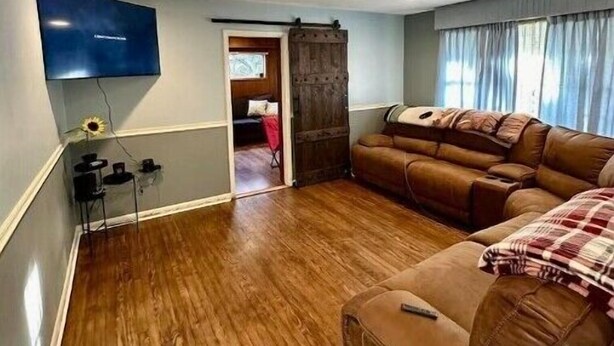 Een woonkamer met een bruine leren bank, een flatscreen televisie aan de muur en een houten vloer.