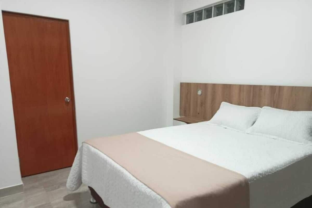 Ein Schlafzimmer mit einem Bett, einem Holz-Kopfteil, einer weißen Wand und einer Holztür.