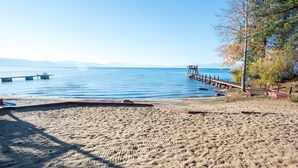 A sandy beach with a pier extending into calm waters, a clear sky, and distant mountains.