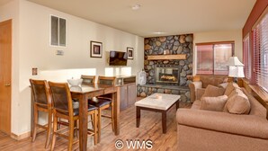 A living room with a stone fireplace, a dining area with wooden furniture, and a sofa with cushions. - Lake/Beach Front Resort - Pool, Hot Tub, BBQ #24 (Tahoe Vista)