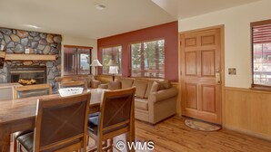 A living room with a stone fireplace, wooden furniture, and large windows with blinds. - Lake/Beach Front Resort - Pool, Hot Tub, BBQ #24 (Tahoe Vista)