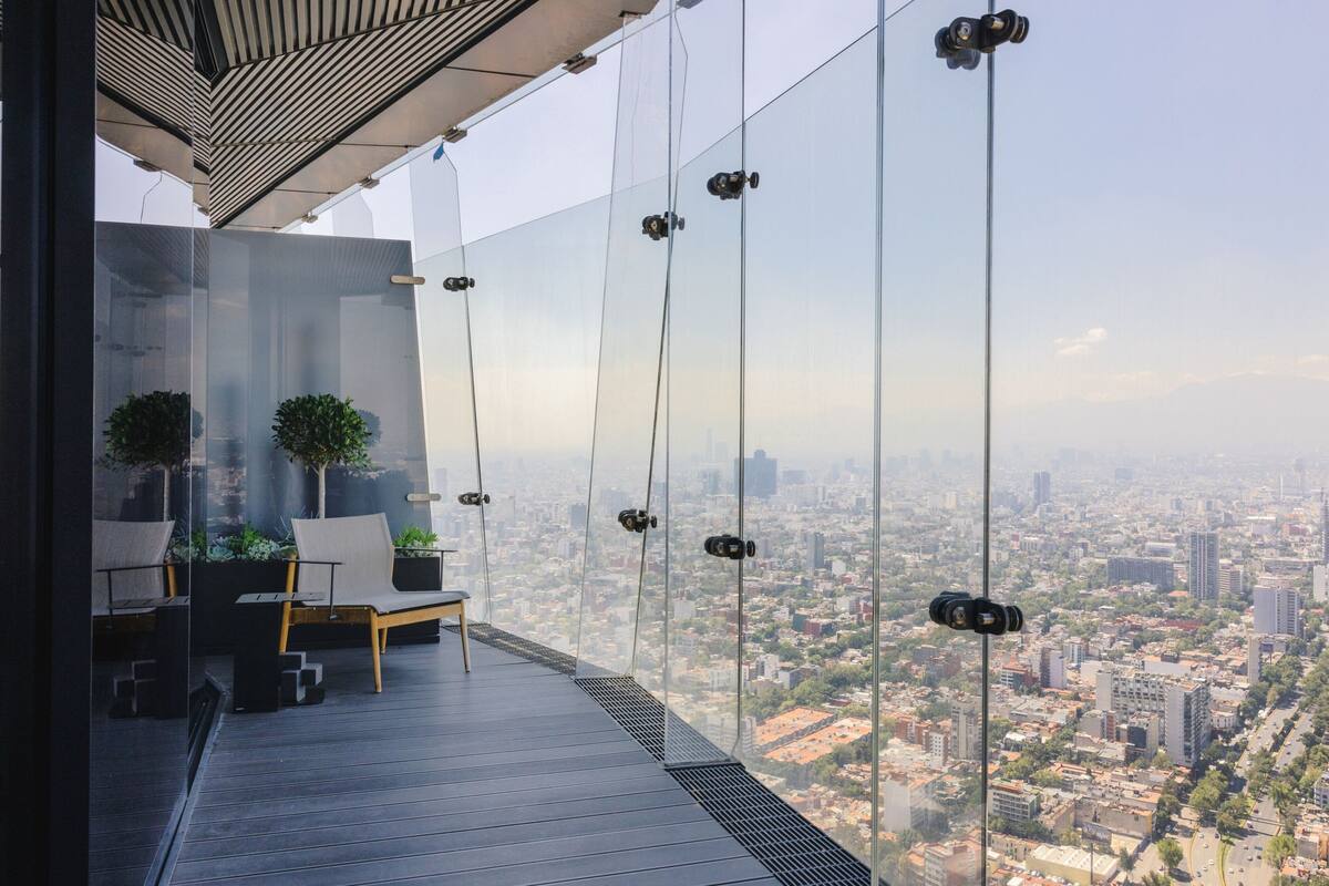 A modern outdoor balcony with a city view, glass railings, and minimalist furniture.