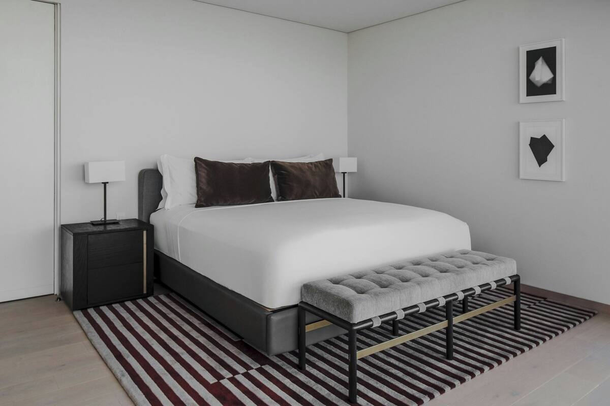 A modern bedroom with a bed, bedside tables, a bench, and a striped rug.