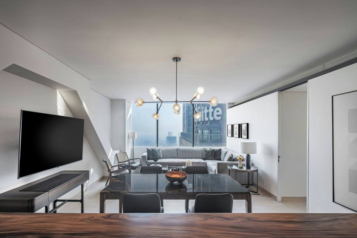 A modern living room with a large flat-screen TV, a dining table, and a sofa set.