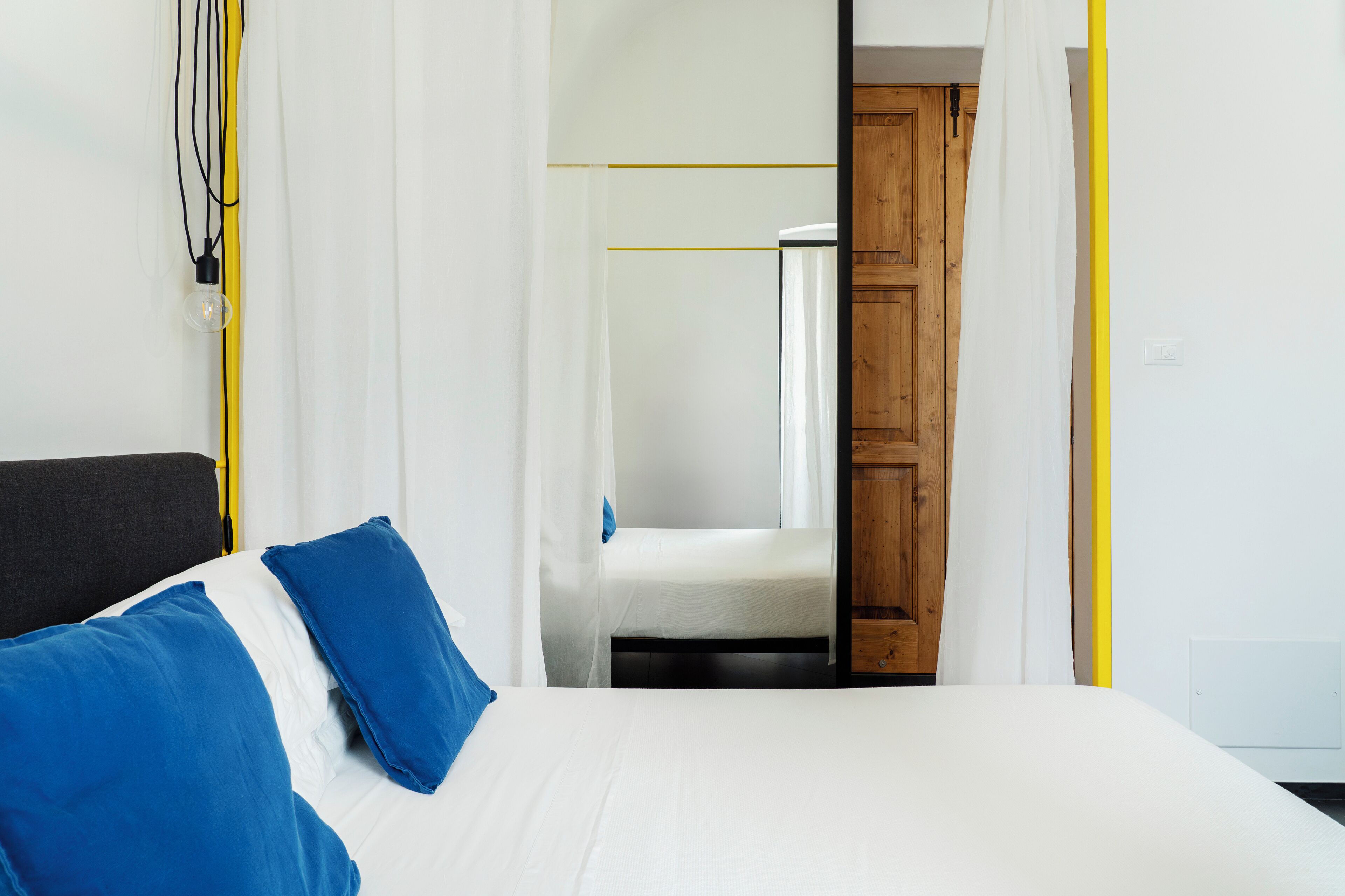 A hotel room with a bed, a wooden door, and a white wall.
