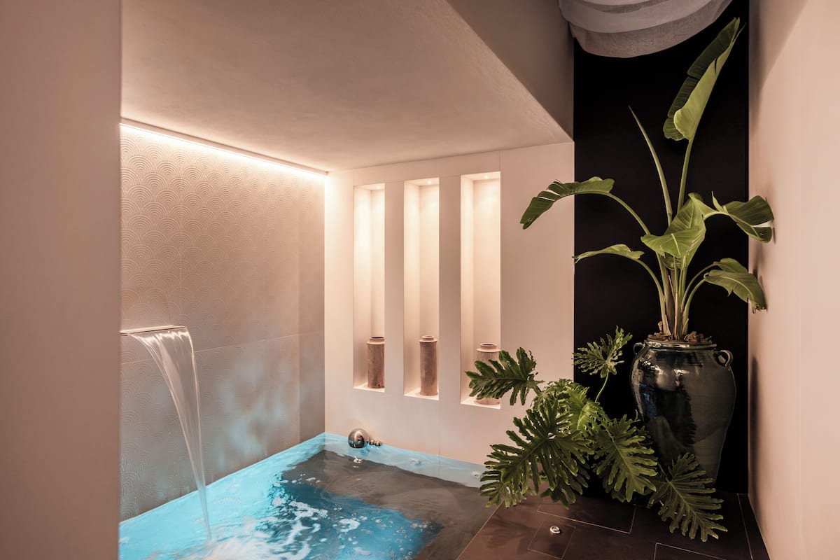 Un baño moderno con un jacuzzi integrado, iluminación empotrada y una gran planta en maceta.