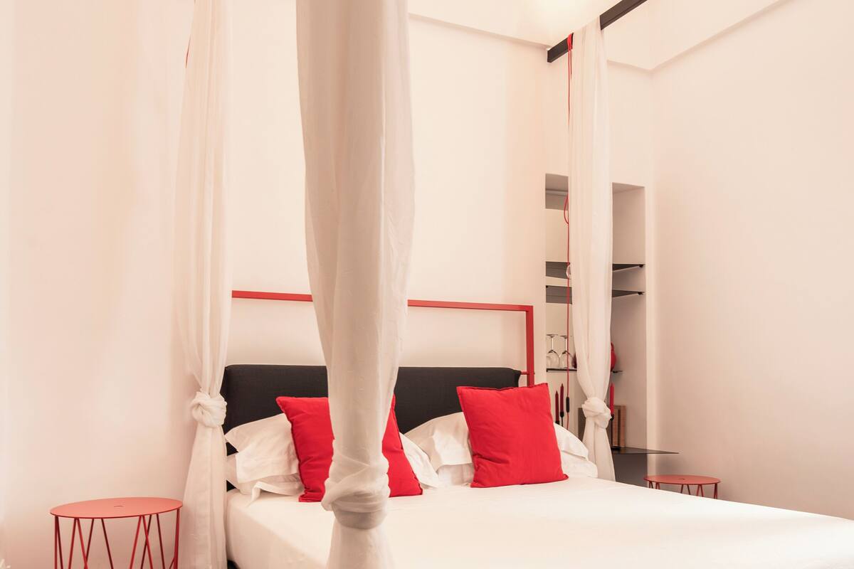 Un dormitorio moderno con cama con dosel, una pared de acento roja y una mesita de noche roja.