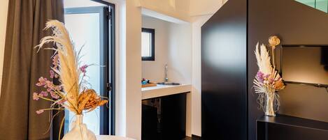 A modern kitchen with a dark countertop, a sink, and a window above the sink. There is a vase with dried flowers on the countertop.