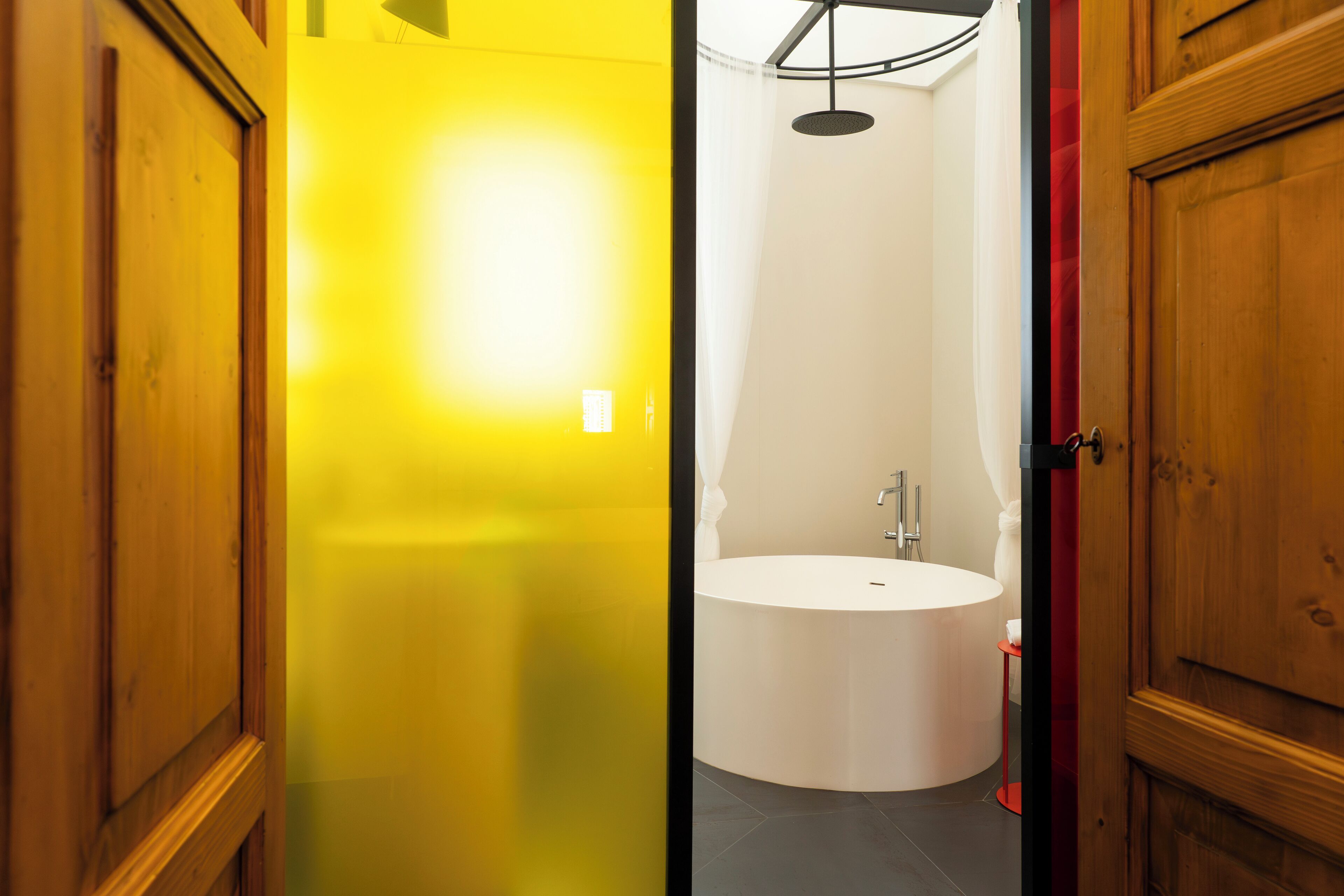 A modern bathroom with a white bathtub, a round mirror, and a ceiling light fixture.