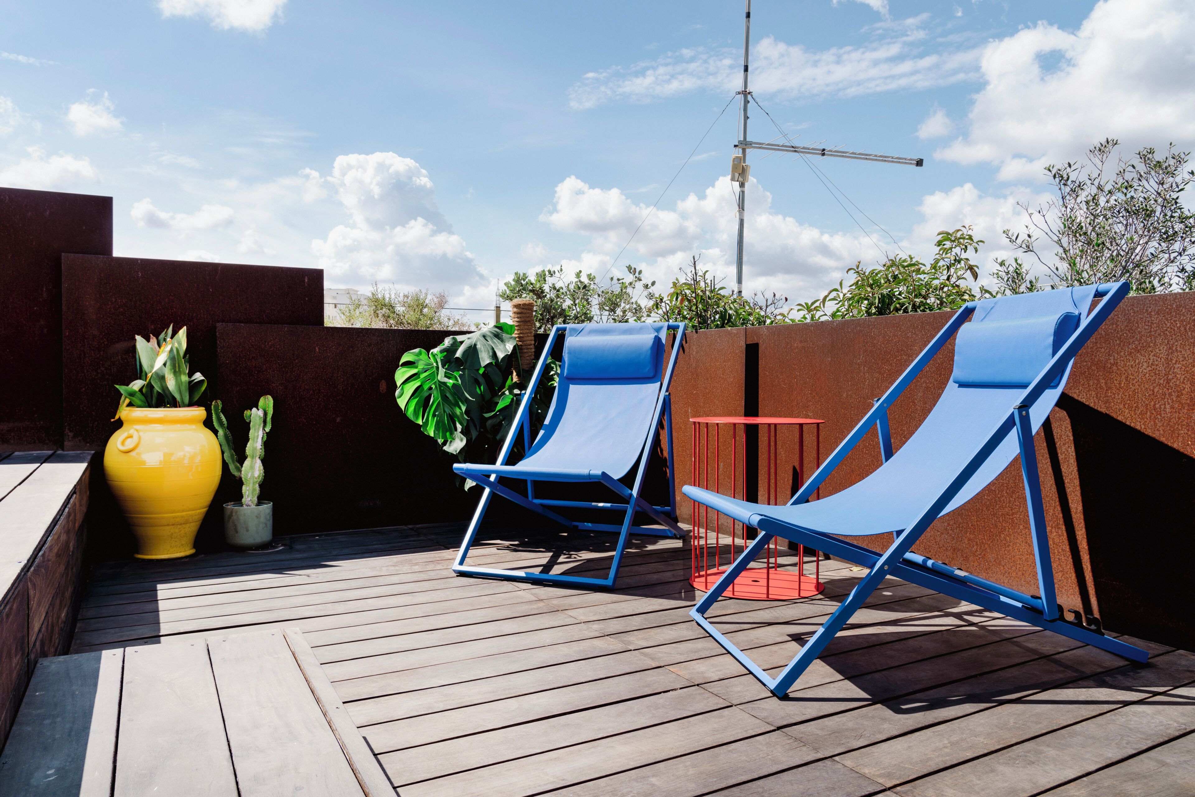 A wooden deck with two blue lounge chairs and a yellow pot with plants.