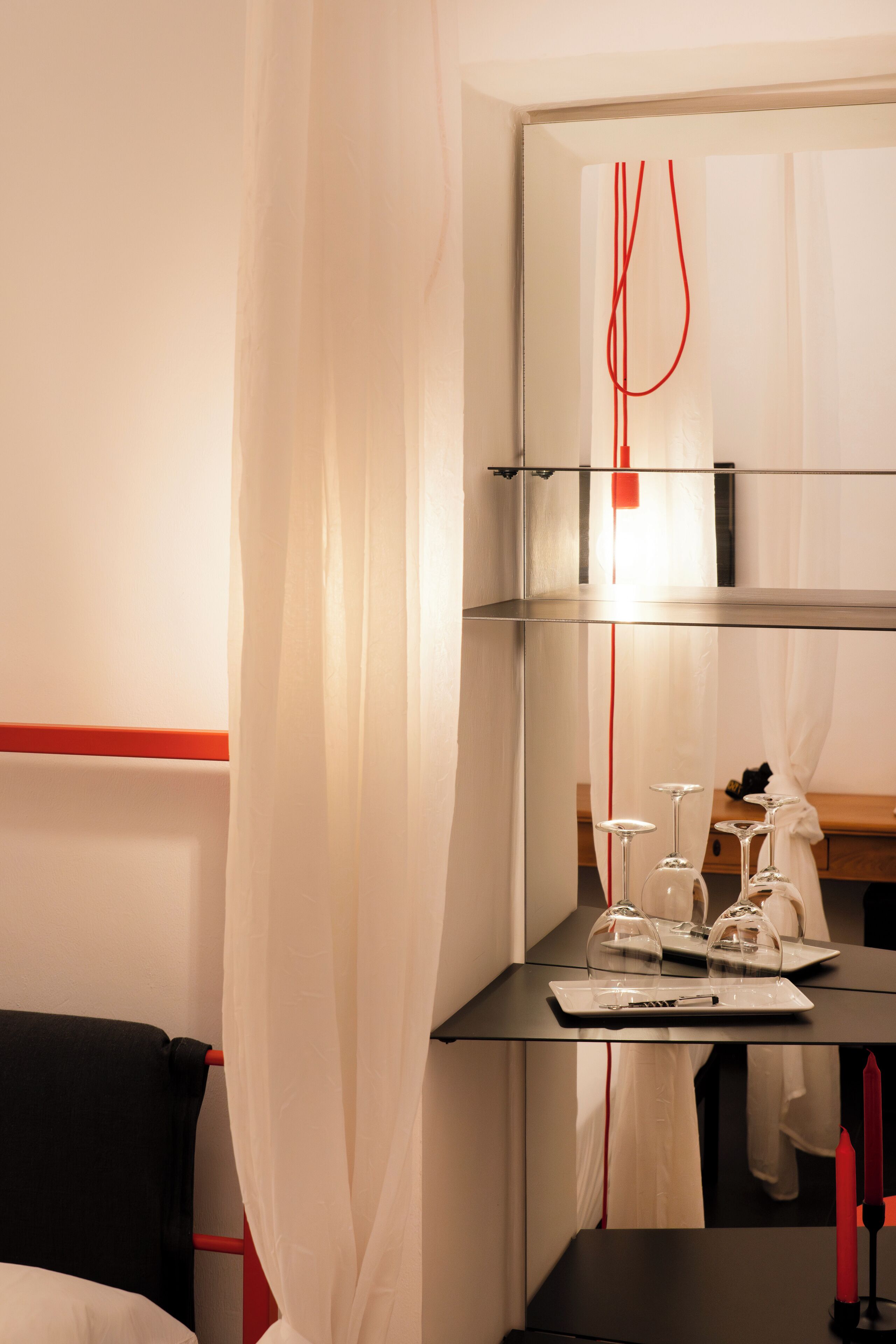 A hotel room with a bed, a table with wine glasses and a candle, and a mirror with a red light.