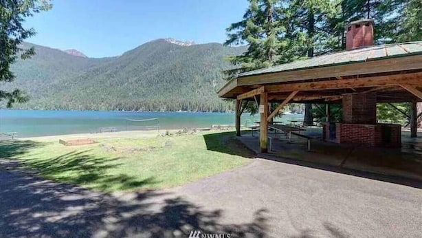 A wooden pavilion with a brick chimney, overlooking a lake and mountains.