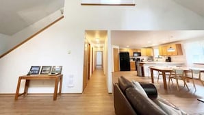 A modern loft-style apartment with a high ceiling, wooden flooring, a dining area with a table and chairs, a kitchen with wooden cabinets, and a living area with a sofa.