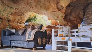 A cave-like interior with a sofa and a white side table with patterned cushions. - Cave Diani Studio Apartments (Diani Beach)