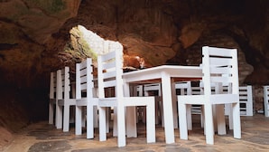 A set of white tables and chairs arranged in a cave-like setting with stone walls. - Cave Diani Studio Apartments (Diani Beach)