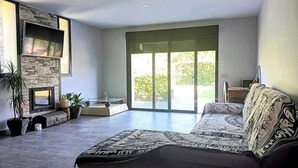 Een moderne woonkamer met een grote bank, een open haard, een flatscreen-televisie en een schuifpui naar een balkon.