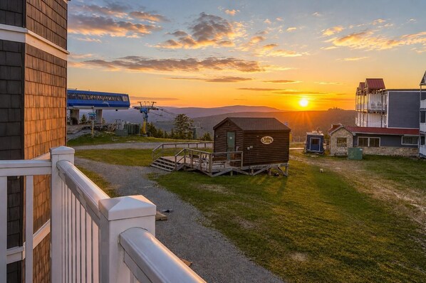 Una cabaña con terraza de madera, un porche pequeño y vistas al atardecer.