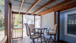 Een overdekt terras met een houten tafel en stoelen, uitzicht op de achtertuin en een garagepoort.