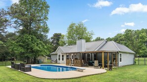 Een huis met een zwembad, overdekt terras en omheinde tuin.