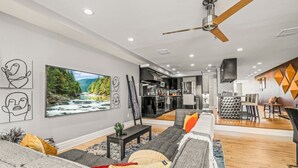 A modern living room with a large TV, grey sofa, and a dining area with a geometric wall design. - Rare Indoor Heated Pool + Philly Rooftop Deck (Philadelphia)
