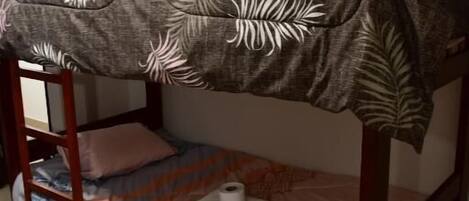 A bunk bed with a leaf-patterned bedspread, a pink mattress, and a wooden ladder.