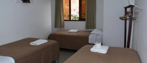 Habitación de hotel con dos camas individuales, una ventana con cortinas, perchero y estante con artículos de aseo.