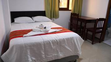 Una cama bien hecha con un edredón a rayas, una pequeña mesa con sillas y una ventana con cortinas.