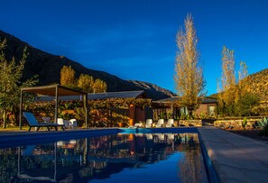 A pool area with lounge chairs and a pergola, surrounded by cacti and trees, with mountains in the background. - Casa de huéspedes Chañarmuyo (Chañarmuyo)