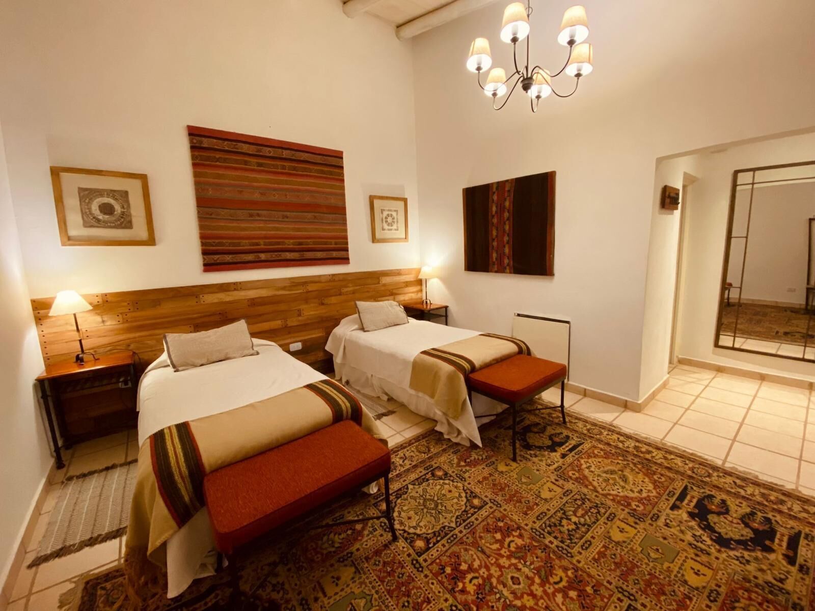 A hotel room with two beds, a large rug, a chandelier, and artwork on the walls.