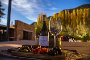 A bottle of wine and a glass on a wooden board with olives and cured meats. - Casa de huéspedes Chañarmuyo (Chañarmuyo)