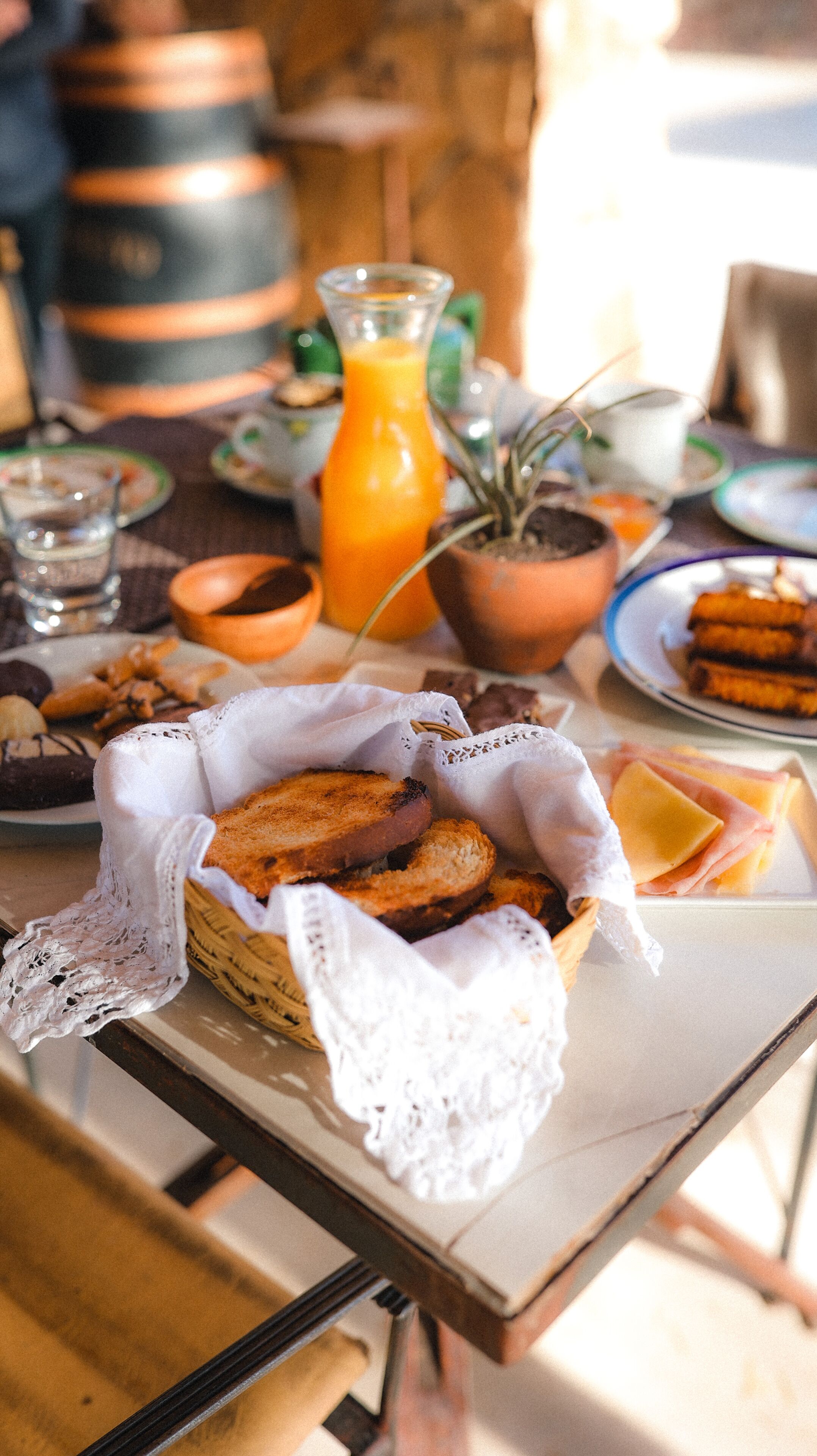 A table with a basket of bread, a glass of orange juice, and various plates of food.